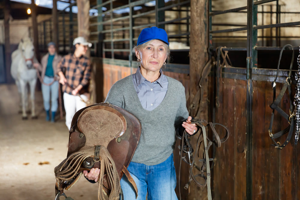 Female rancher carrying horse tack and saddle in horse farm