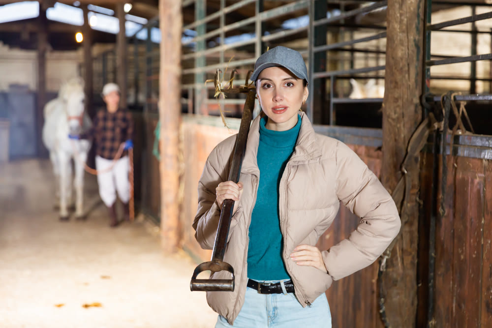 Woman with pitchfork standing in horse barn