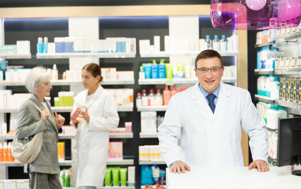 At pharmacy, man apothecary waiting for clients and invites with gesture go to chemist shop