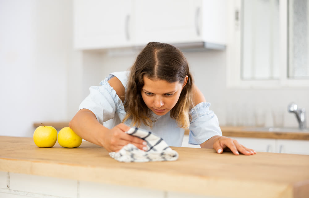 Positive woman cleaning kitchen table at home