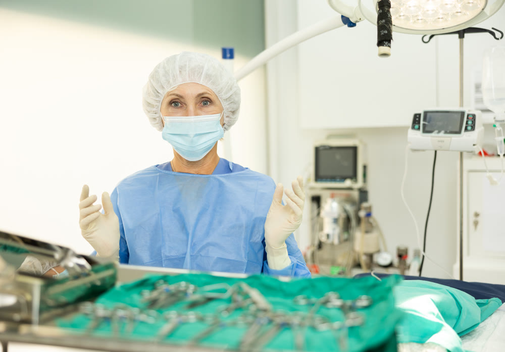 Mature woman doctor in entire perfect surgical suit stands with raised hands in gloves