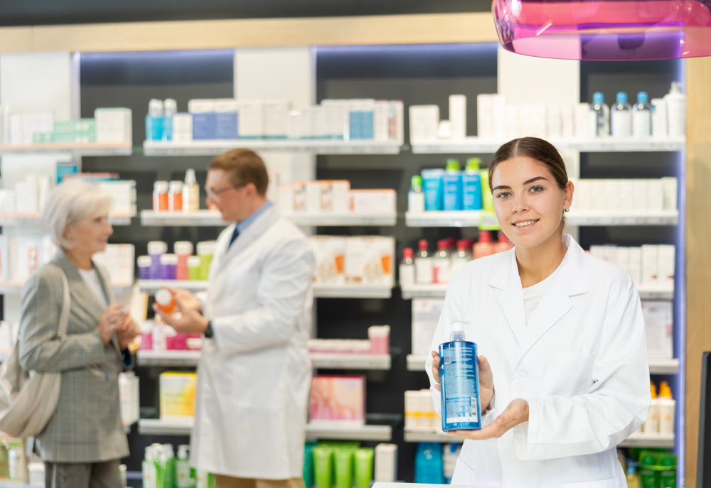 Female pharmacist in medical uniform posing with product intimate hygiene in her hands in pharmacy
