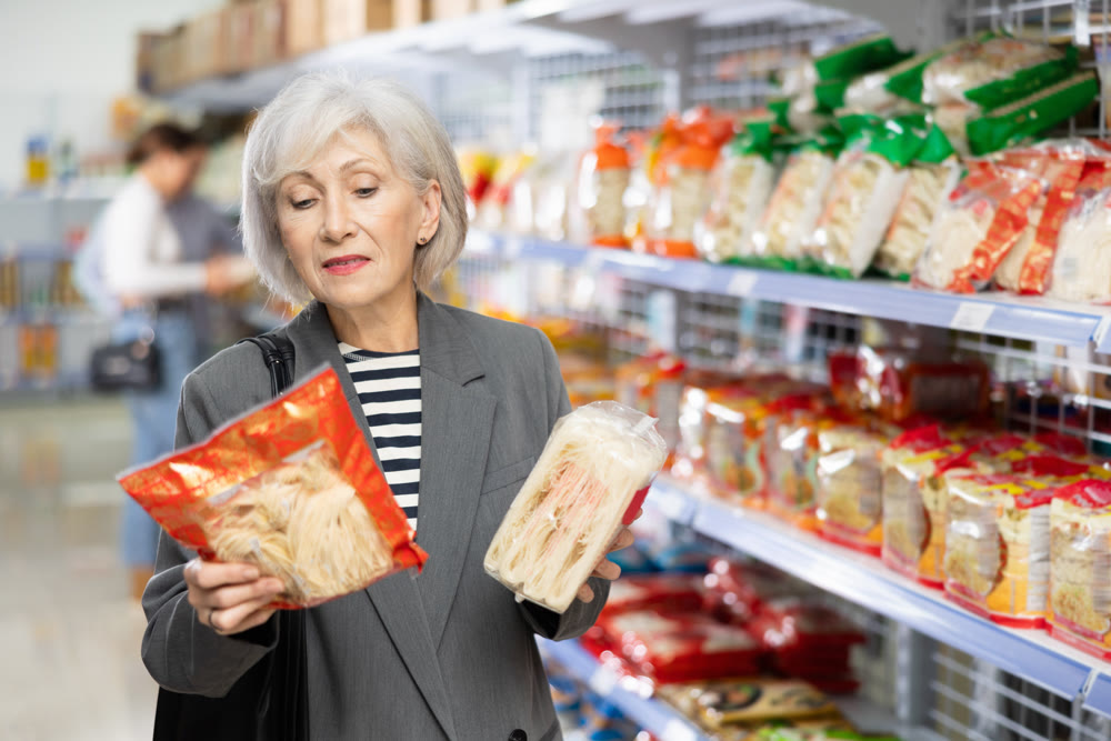 Senior woman in supermarket buys daily groceries, pasta Chinese noodles