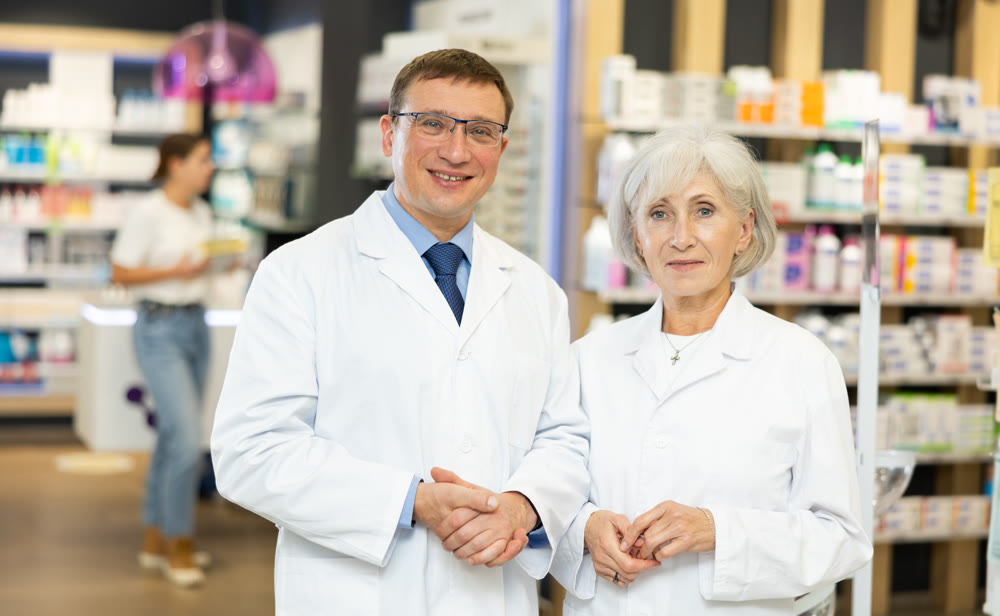 Middle-aged man and mature woman pharmacists posing together in chemist's shop