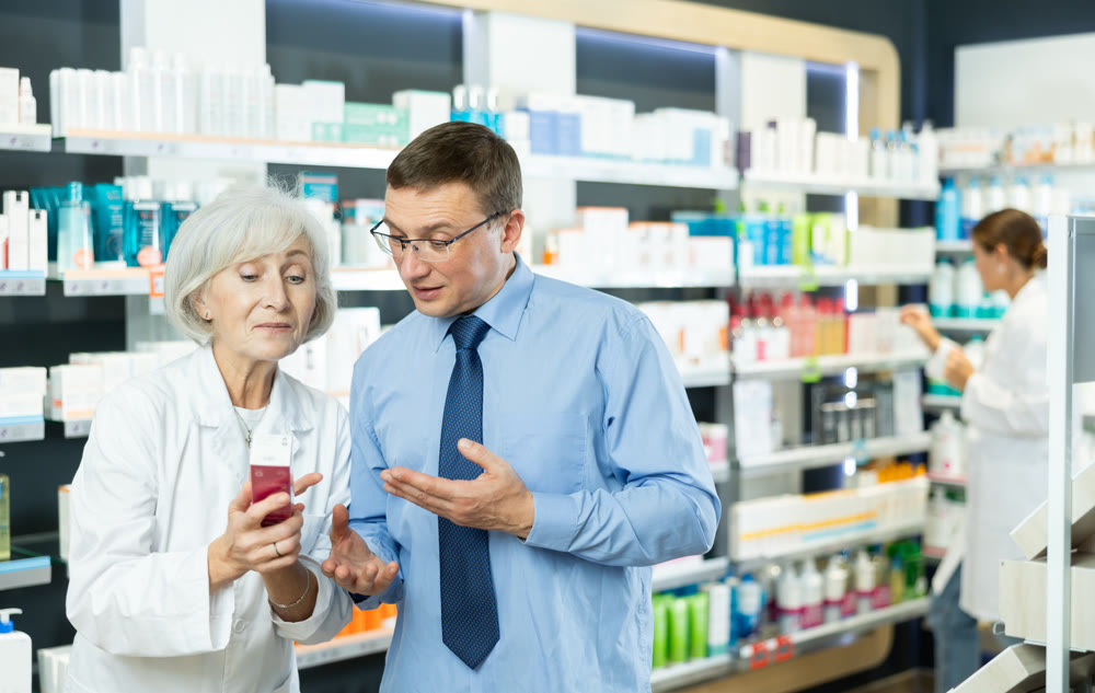 Male customer consulting with mature female pharmacist at pharmacy