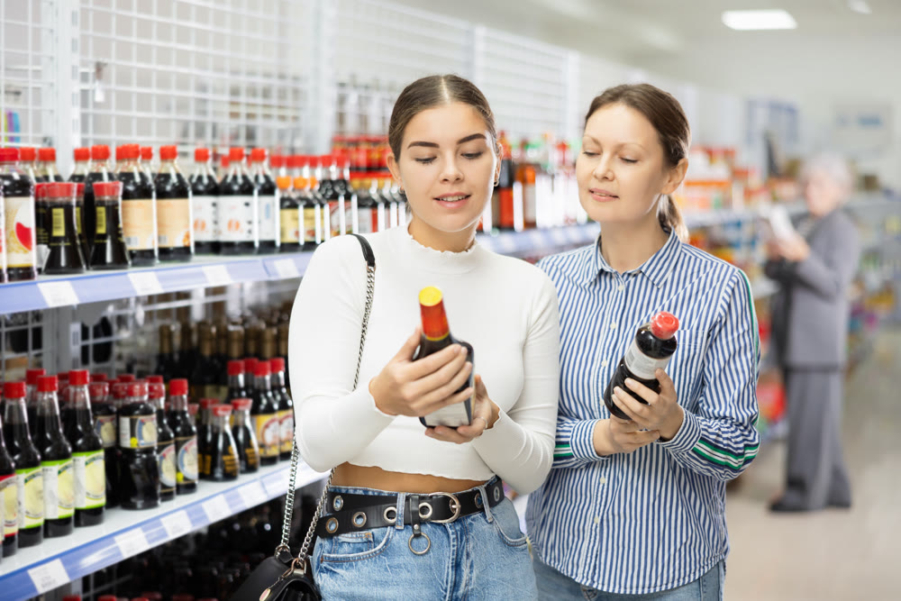 Girl customer with female friend is thinking about buying spicy and unusual soy sauce.