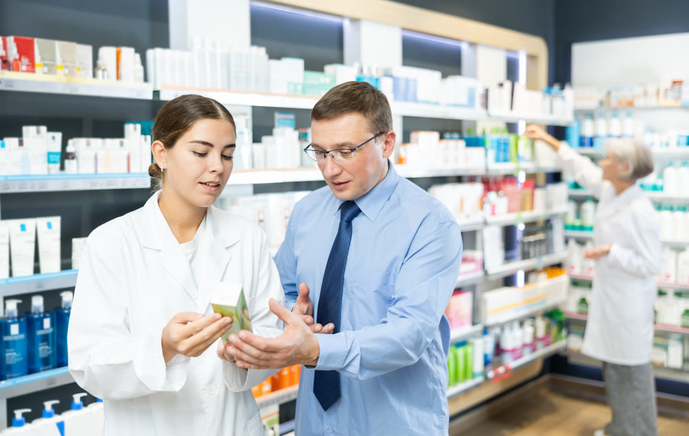 Girl pharmacist gives advice to man what medicinal ointment to buy