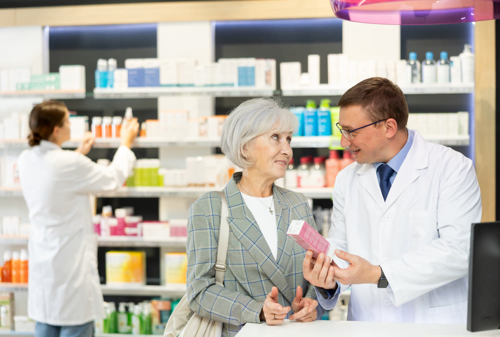 Man apothecary hold package with cream and talks with senior woman client about nuances of care