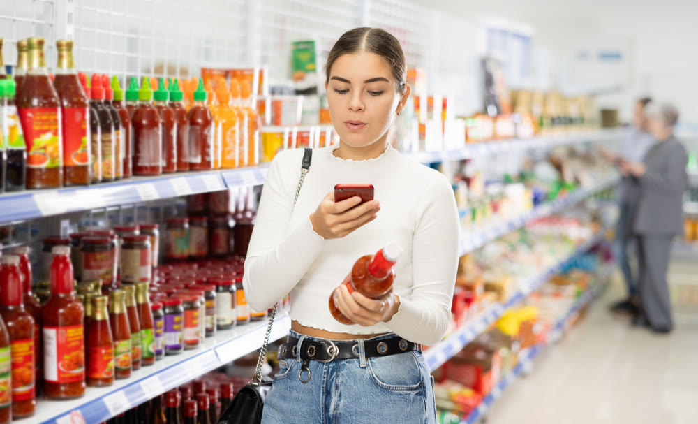 Young girl scanning barcode with smartphone on bottle of sauce in store