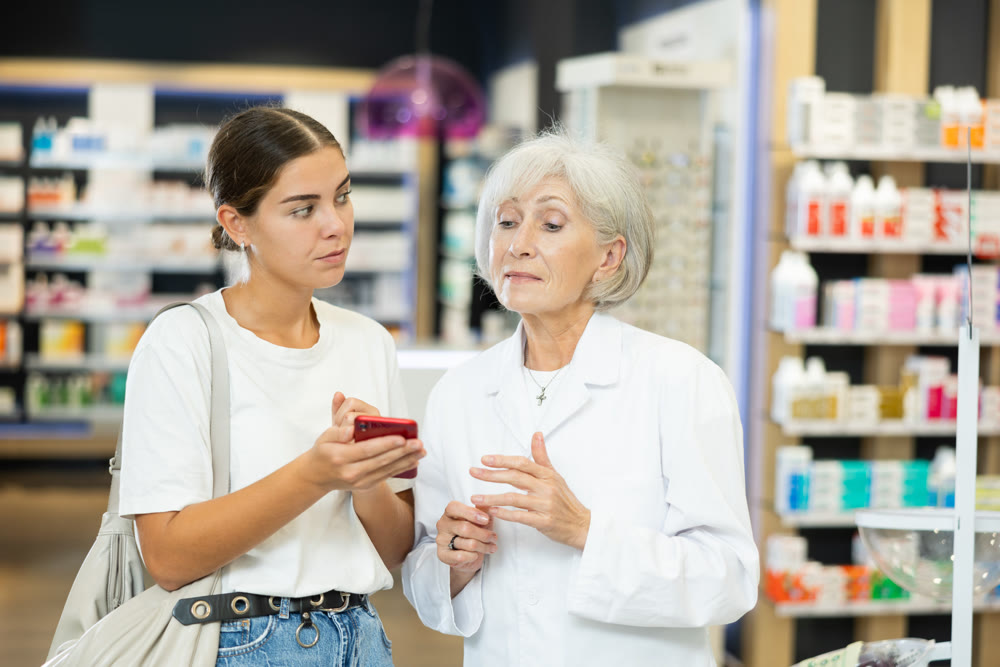 Young girl showing to old pharmacist something displayed on her smartphone