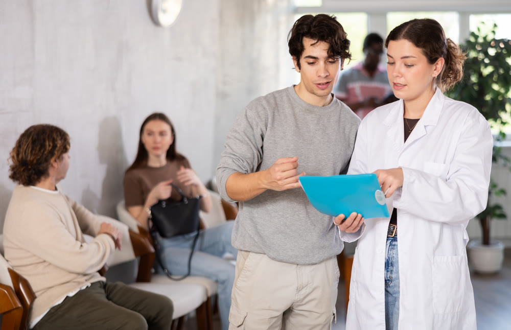 Young female nurse or doctor talking with young guy in reception area
