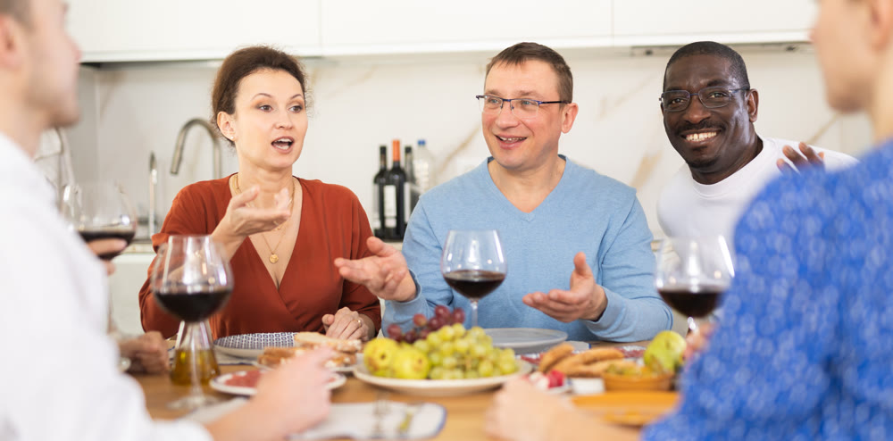 Middle-aged friends sitting at table with a glass of wine while having friendly conversation