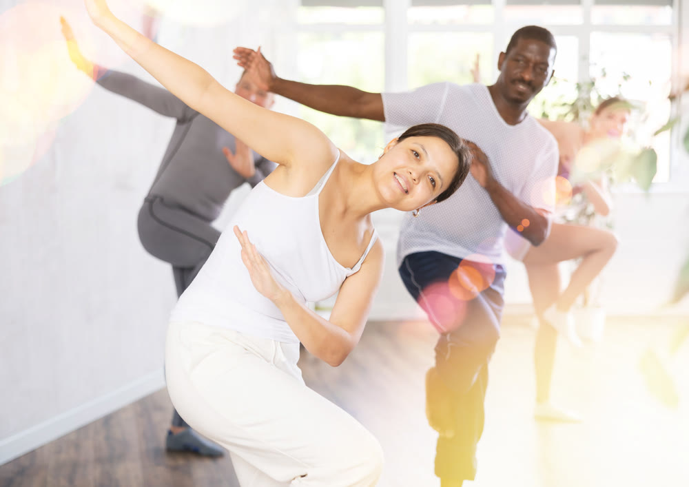 Group of happy sports woman and men in activewear exercising dynamic dancing movemens in gym studio