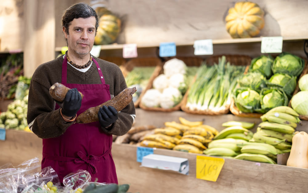 Adult man seller with cassava in vegetable shop