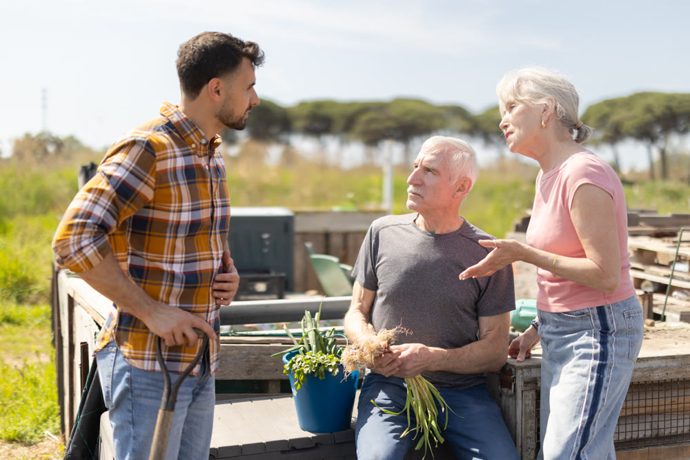 Mature couple and man argue with each other while standing near fence on small farm