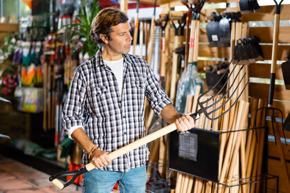 Adult gardener choosing pitchfork in garden tools store