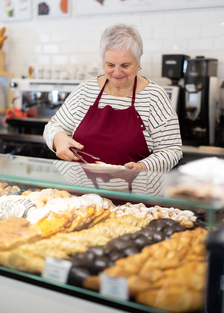 elderly woman works in a bakery and offers pastries