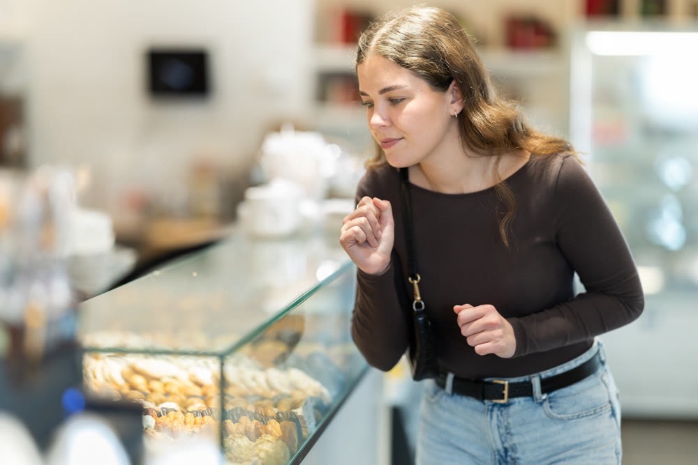 Young woman in casual clothes choosing sweet pastries at pastry shop display