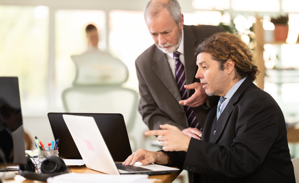 Mature manager helping to man during working at laptop in office
