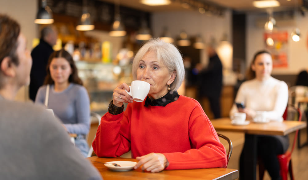 Senior woman in cafe sits opposite male companion, has nice conversation