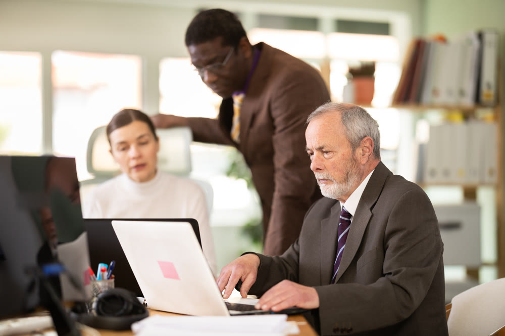 Mature man works online with a team of managers in company office.