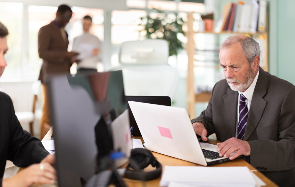 Mature man works online with a team of managers in company office.