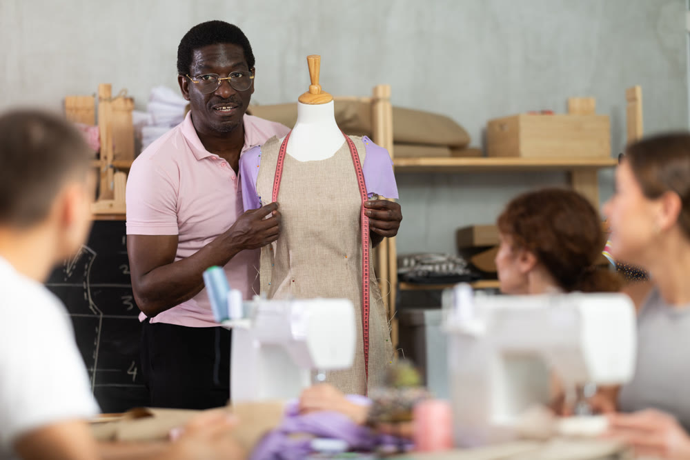 Sewing school African man teacher conducts lesson for students using mannequin
