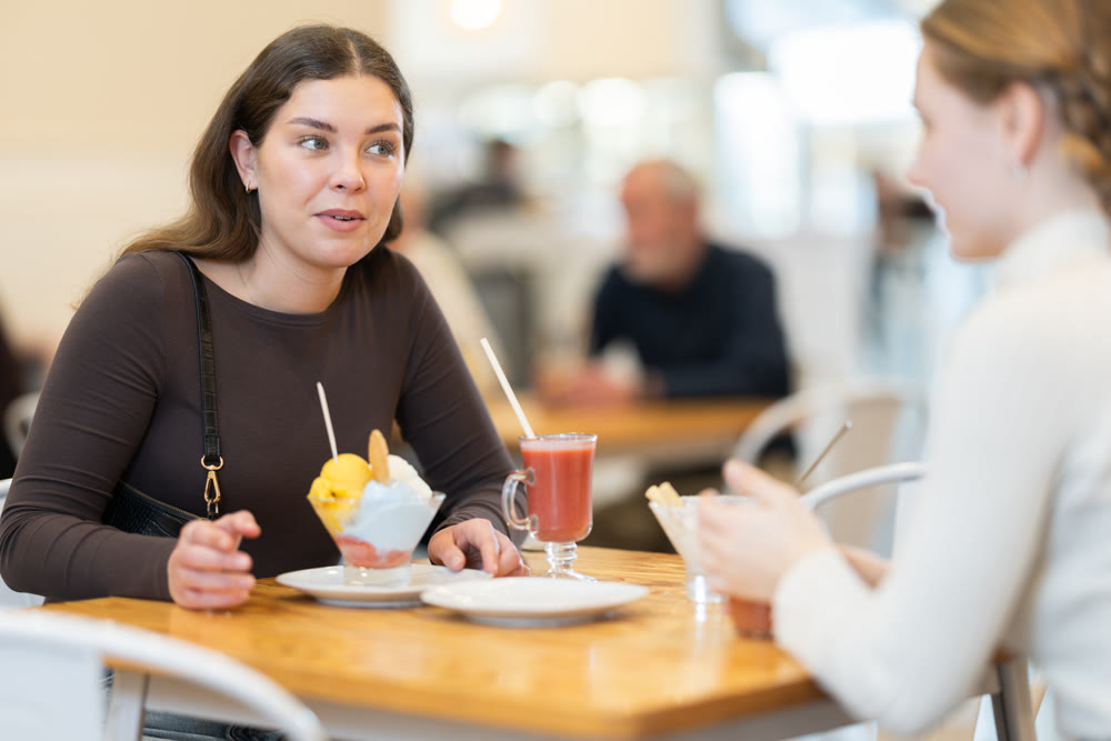 Young woman with teen girl chatting and gossip while drink latte coffee, eating ice cream