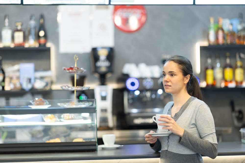 young woman stands at the counter in a cafe and drinks coffee