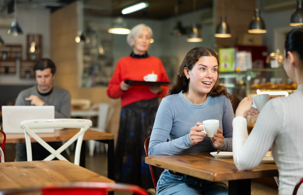 Girl in cafe sits opposite female companion, has nice conversation