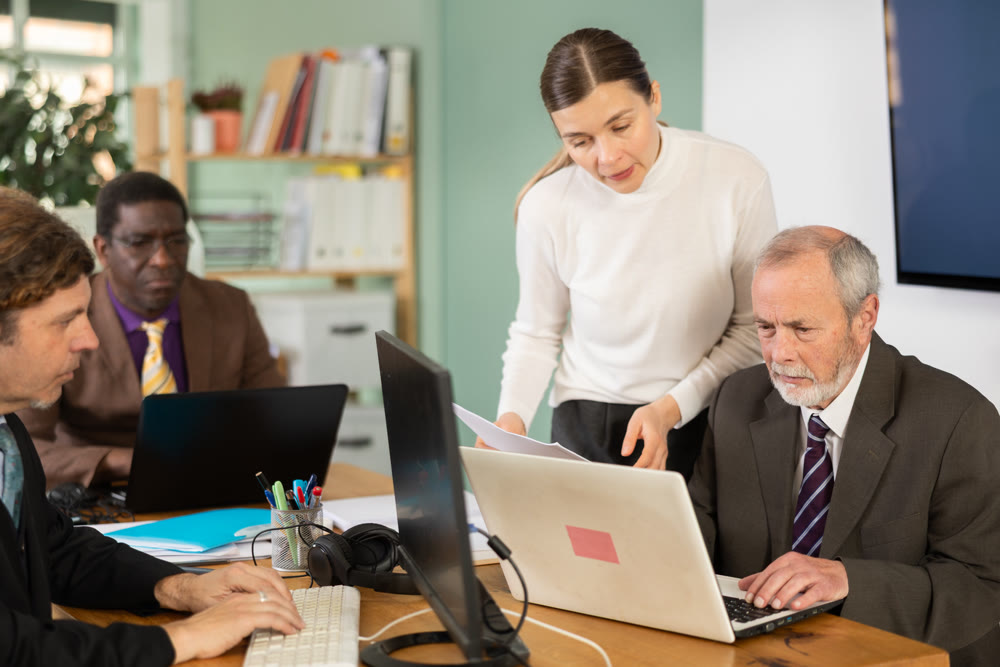 Woman manager helping to elderly man during working at laptop in office