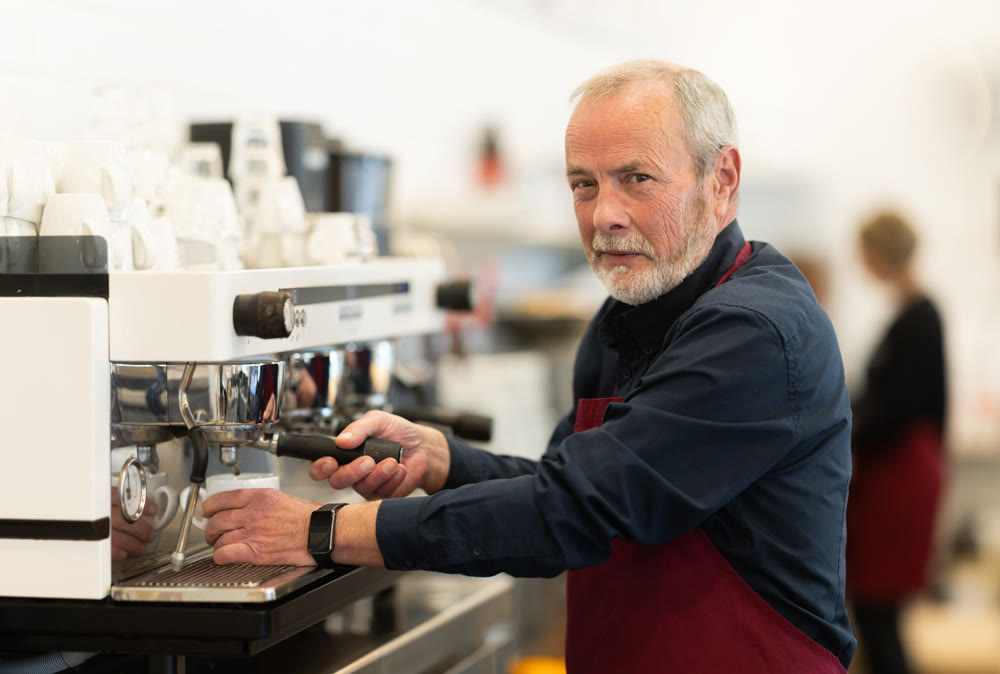 Elderly cafe seller prepares delicious coffee in coffee machine