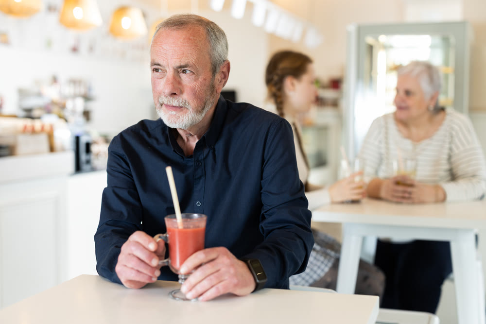 Senior man visitor sits near table, drink juice in chain cafe shop