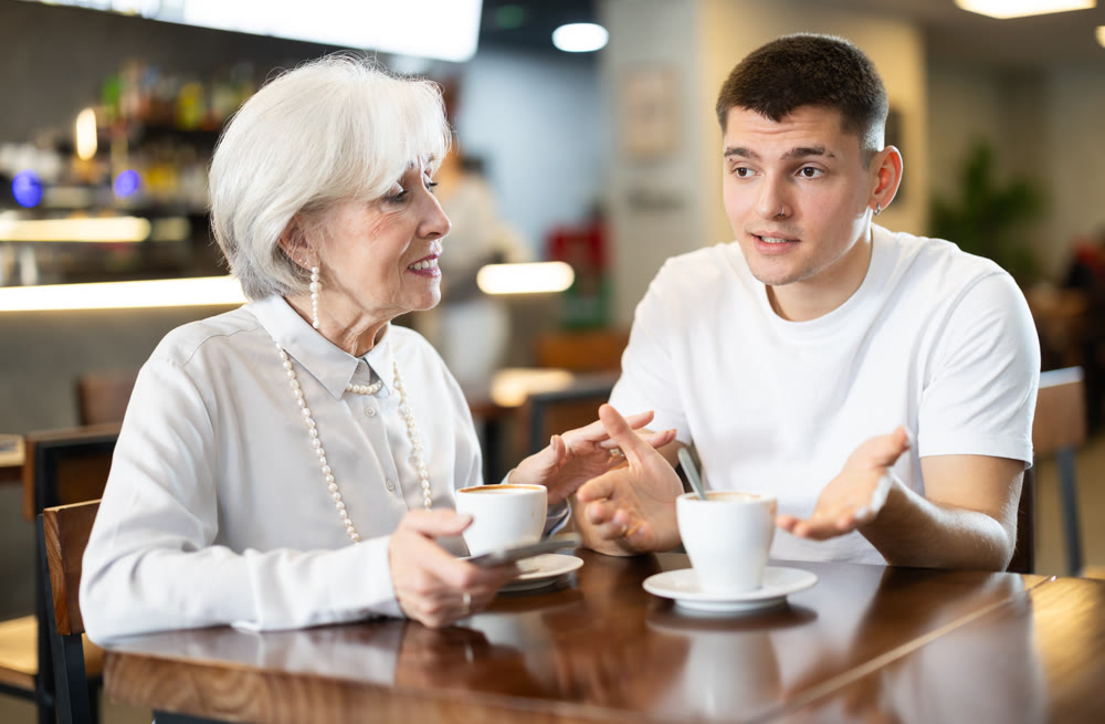 Young man and eldery woman drinking coffee in cafe