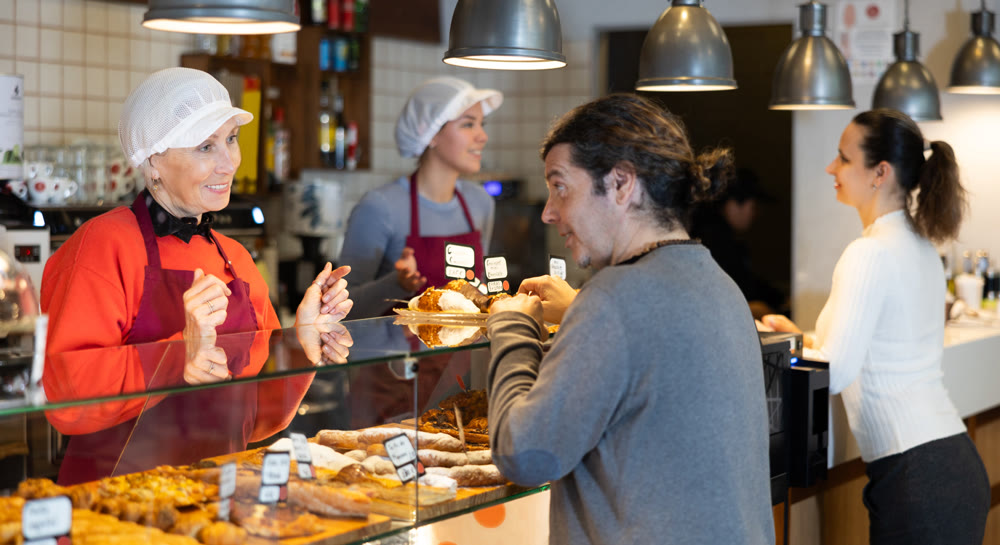 Queue at cafe for delicious pastries. Mature woman seller helps to place an order