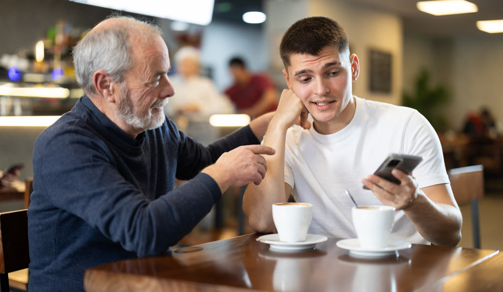 Meeting at cafe. Guy person scrolls down phone screen, elderly man comforts his son