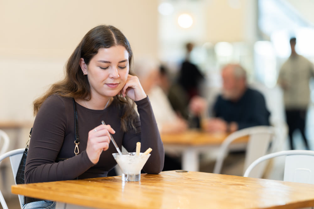 Food court girl visitor sits near table, eating ice cream in chain cafe shop
