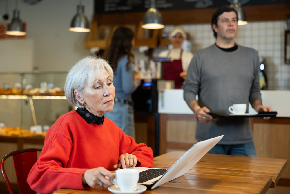 Mature woman sitting at table, using laptop and enjoing cup of tea in coffee house