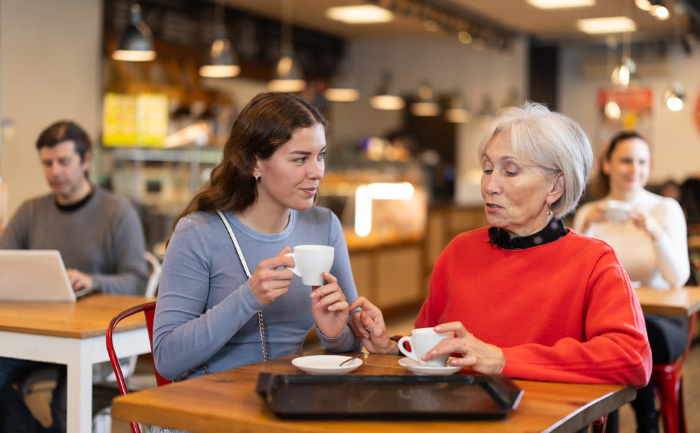Adult daughter talking to mature mother in cafe - drinking tea together