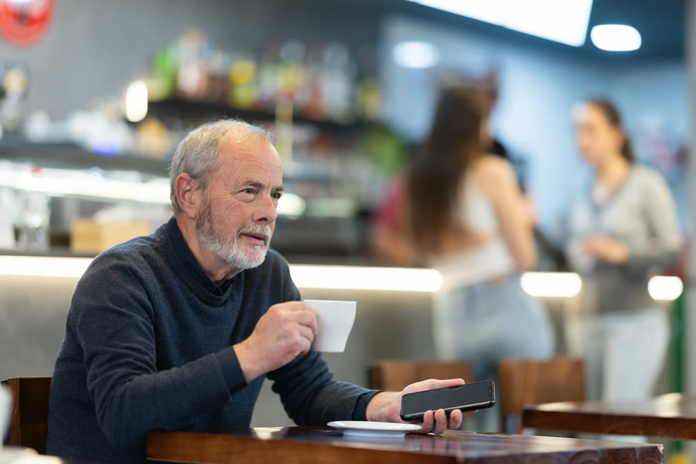 elderly man drinks coffee and holds a mobile phone in his hands