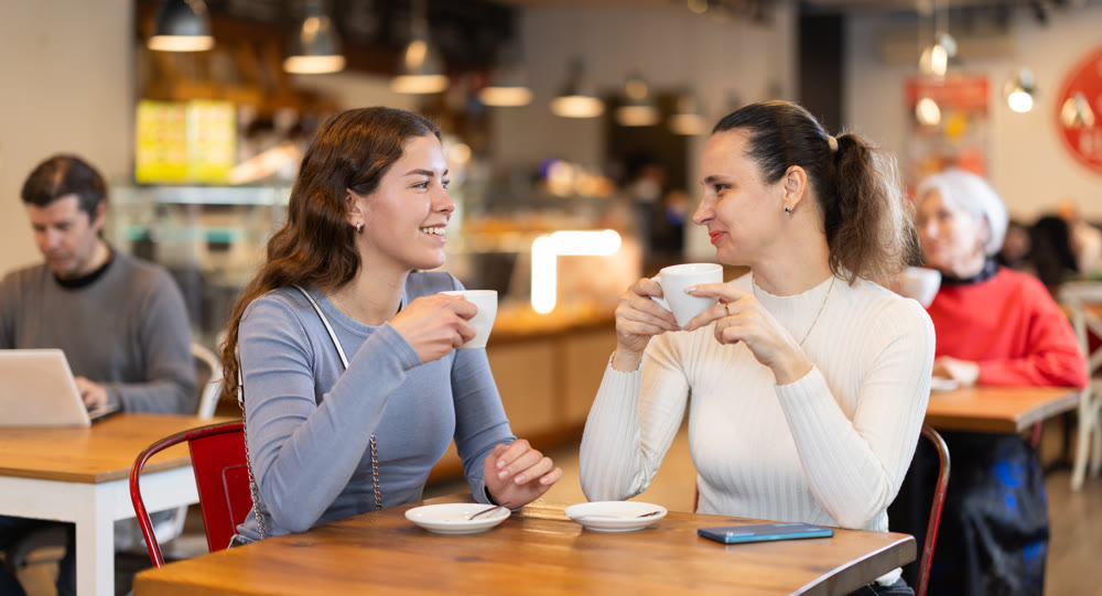 Girlfriends are chatting happily with each other while sitting at table in a cafe and drinking tea