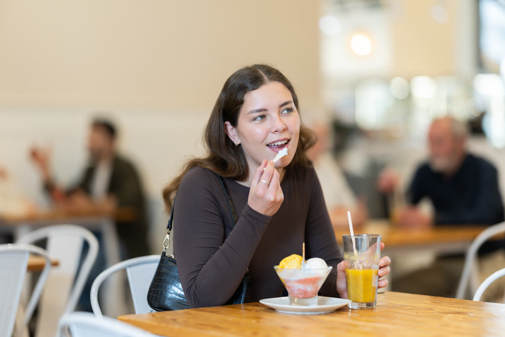 Food court girl visitor sits near table, eating ice cream in chain cafe shop