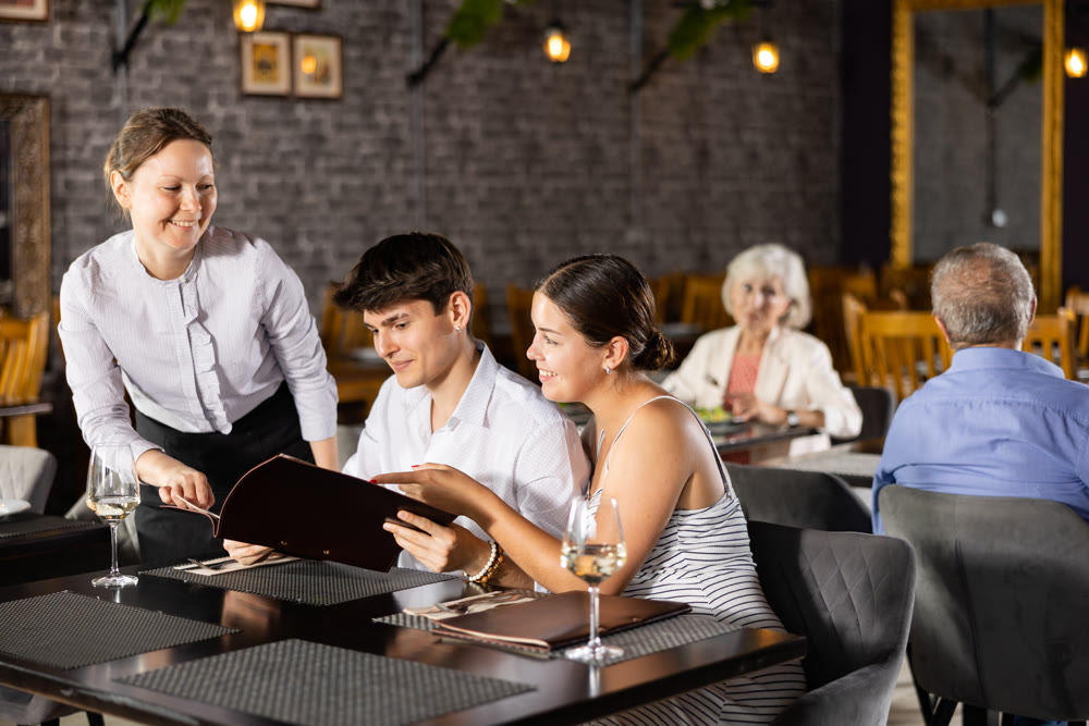 Young couple discussing menu with waitress at table in restaurant