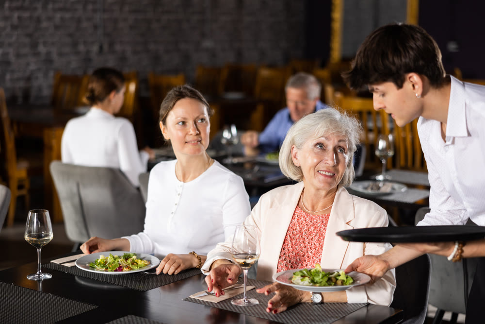 Young waiter serving dishes to female guests in restaurant