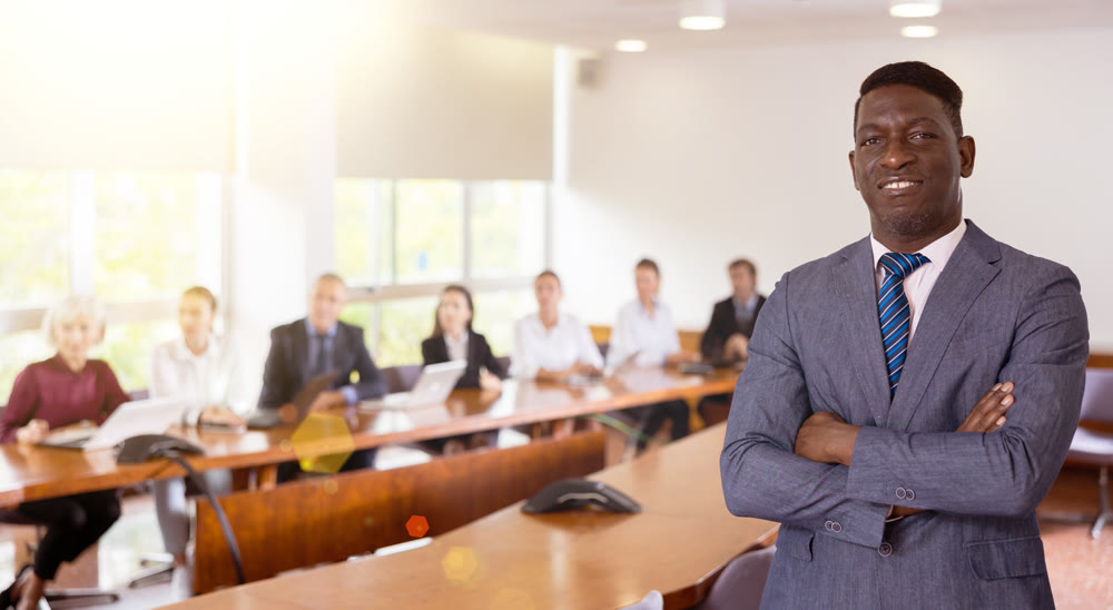 Portrait of successful african american businessman in front of team of businessmen in meeting room