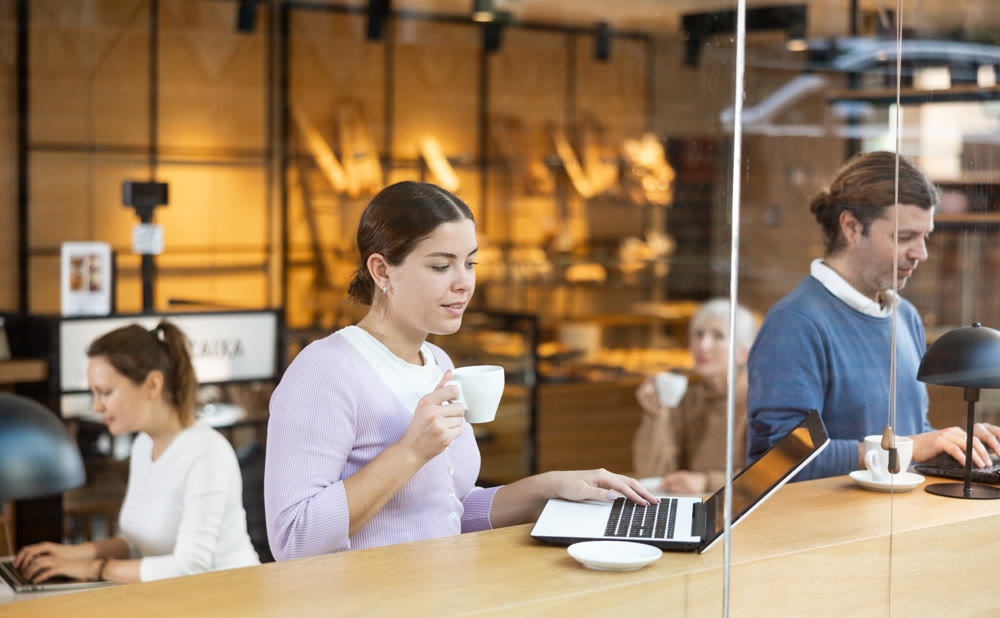 Smiling woman using laptop and drinking coffee in modern cafe