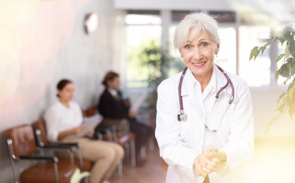 Friendly seniore woman physician standing in office, looking at camera and gesturing