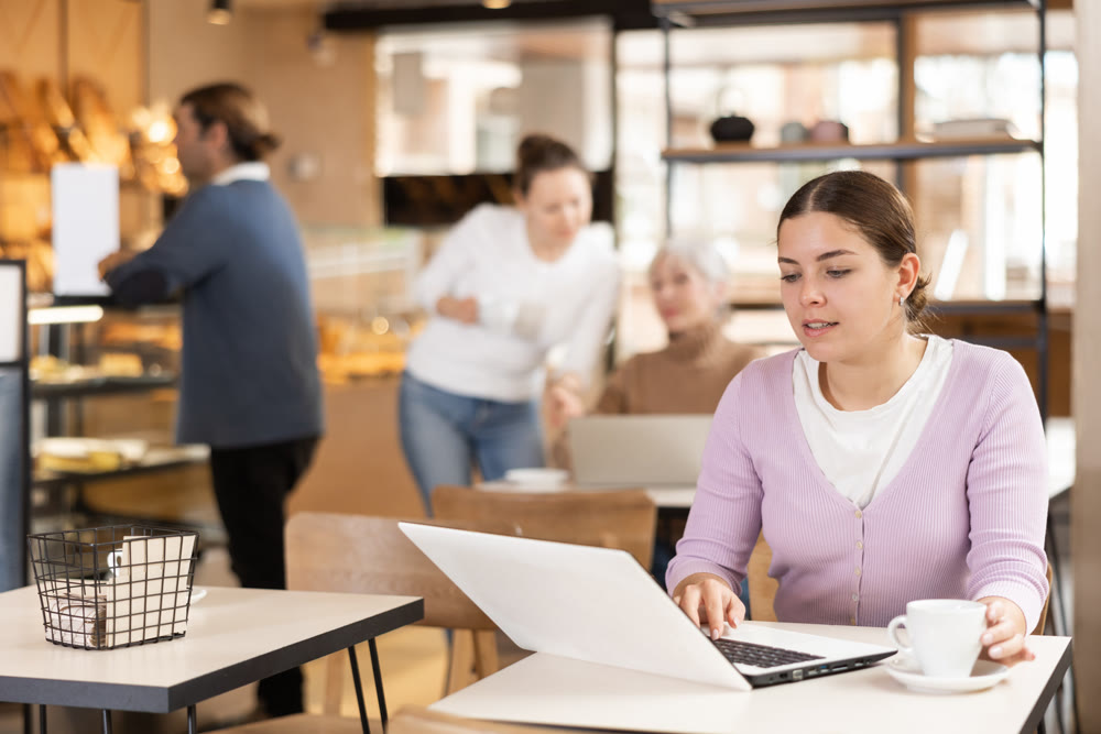 Smiling woman using laptop and drinking coffee in modern cafe