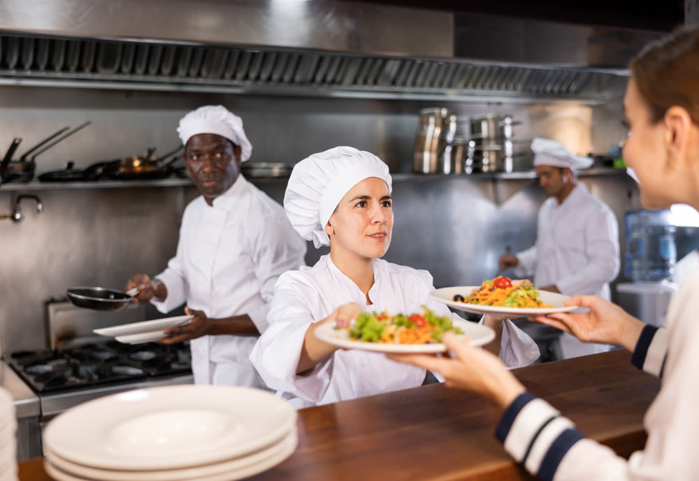 Female chef serving ready meals to visitors of modern restaurant