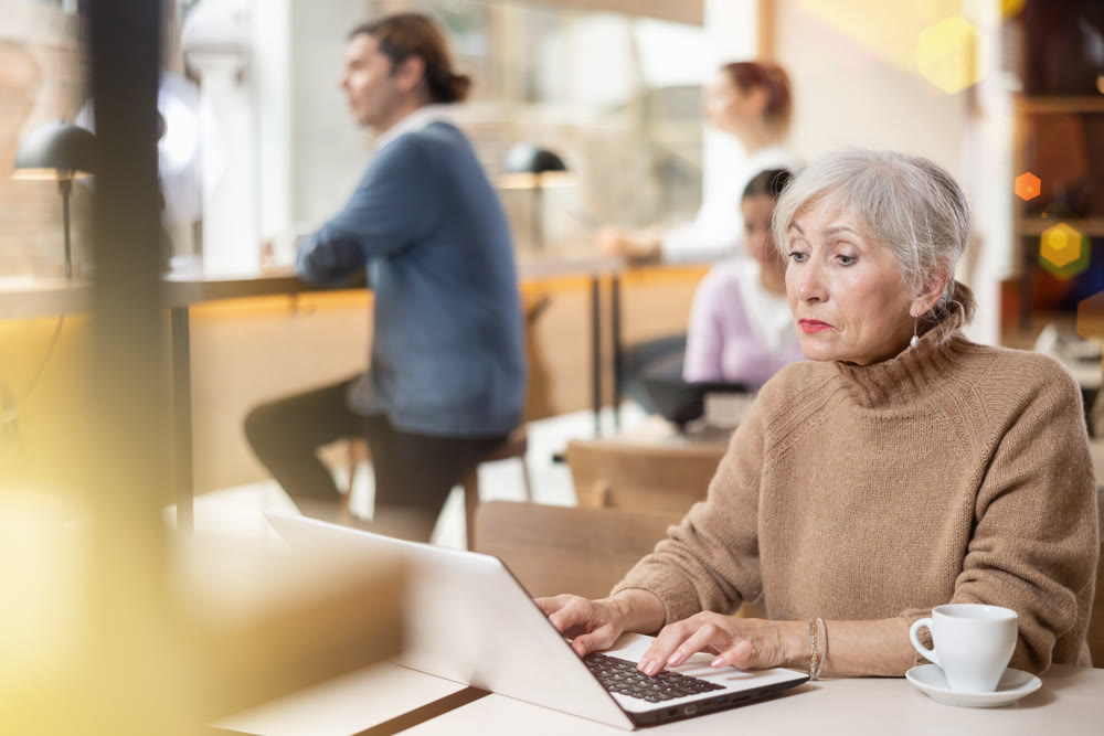 Mature woman spending time in cozy coffeehouse with laptop and coffee